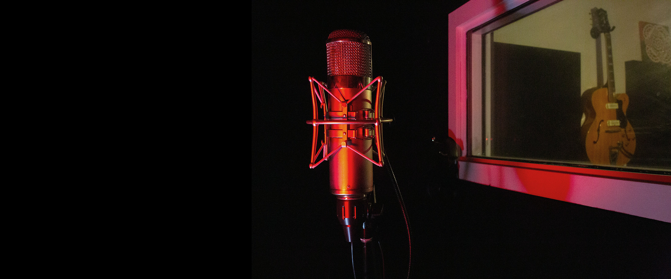 U47 microphone in recording booth, with beautiful guitar visible through booth glass